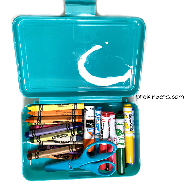 Art supplies in a pencil box: crayons, markers, scissors, glue
